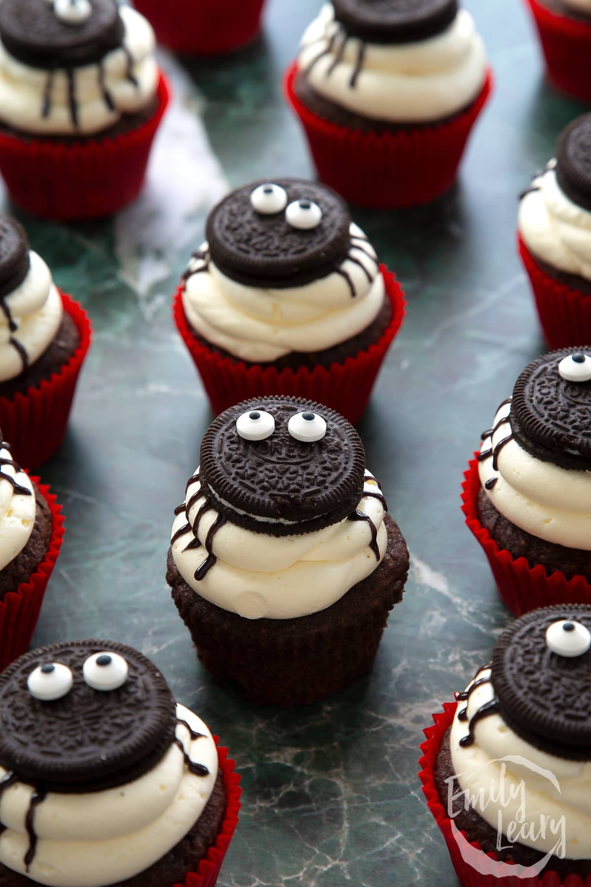 Vegan Halloween cupcakes, decorated with Oreos and candy eyes to look like spiders. One is unwrapped.