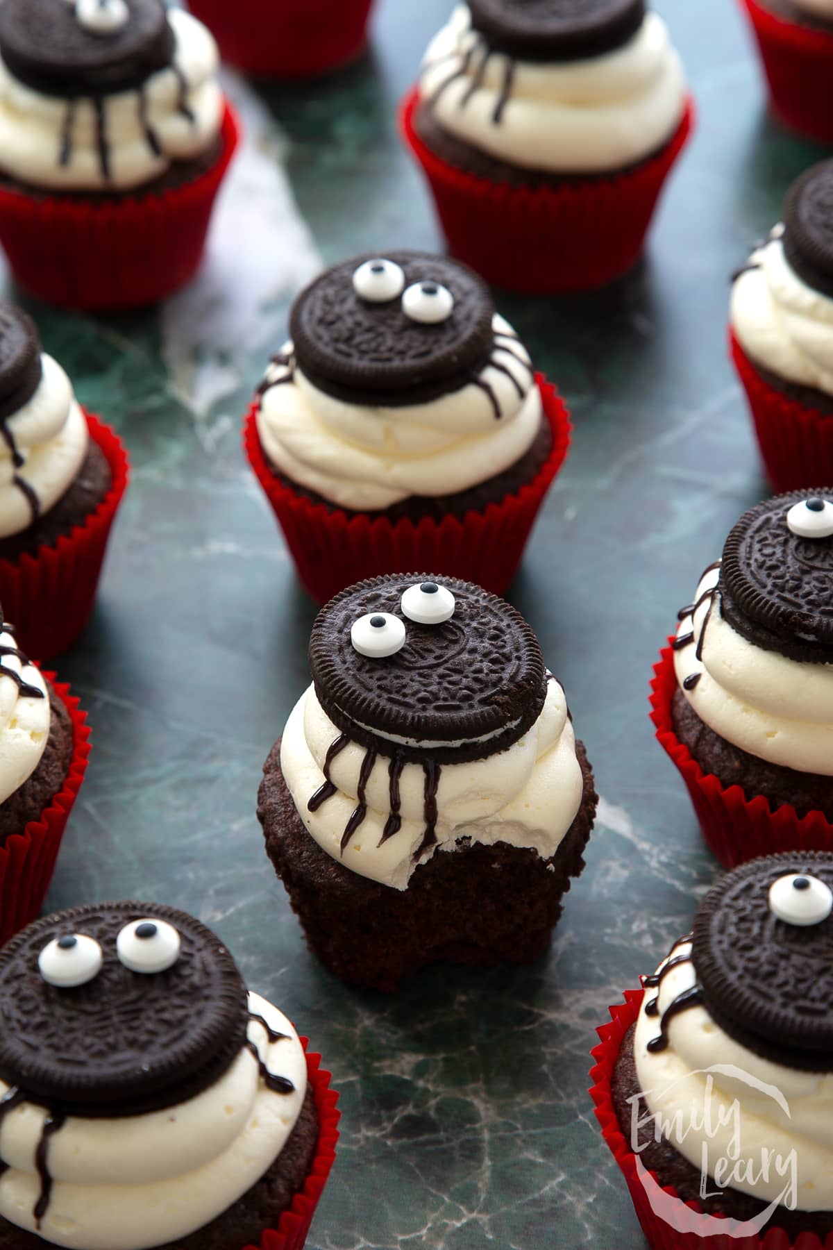 A vegan Halloween cupcake with a bite out of it, decorated with Oreos and candy eyes to look like a spider.