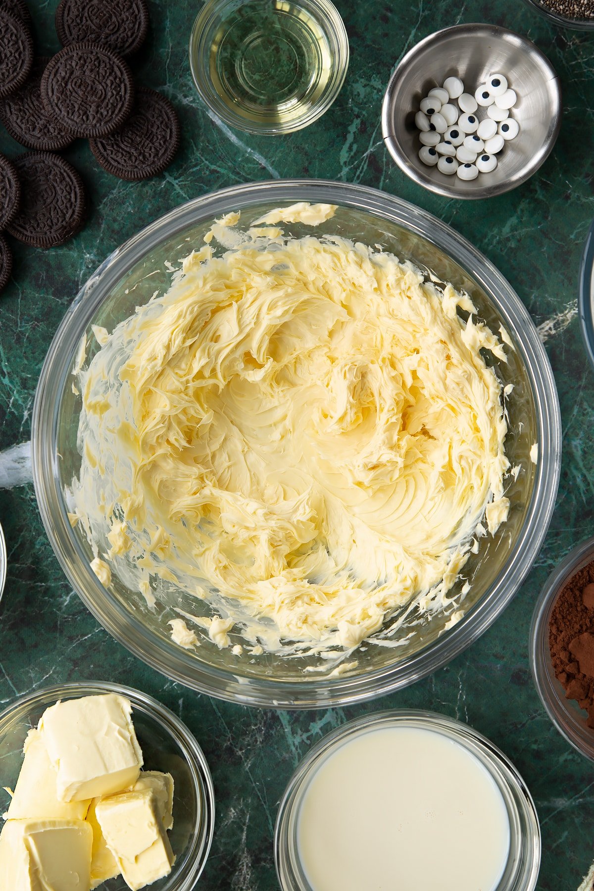 Whipped vegan butter in a glass mixing bowl. Ingredients to make vegan Halloween cupcakes surround the bowl.