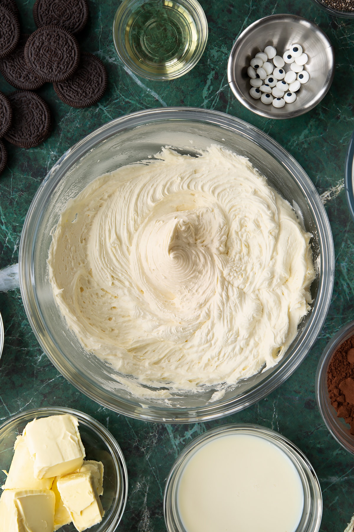 Whipped vegan vanilla frosting in a glass mixing bowl. Ingredients to make vegan Halloween cupcakes surround the bowl.