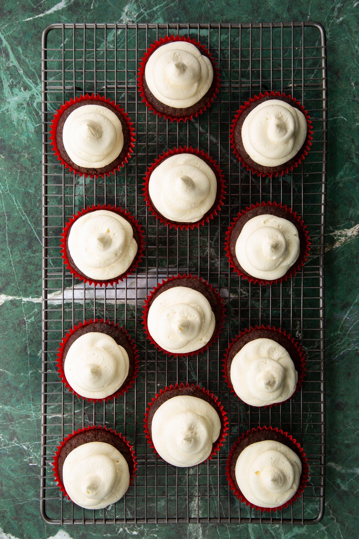 Vegan chocolate cupcakes with vanilla frosting piped on top on a wire cooling rack.