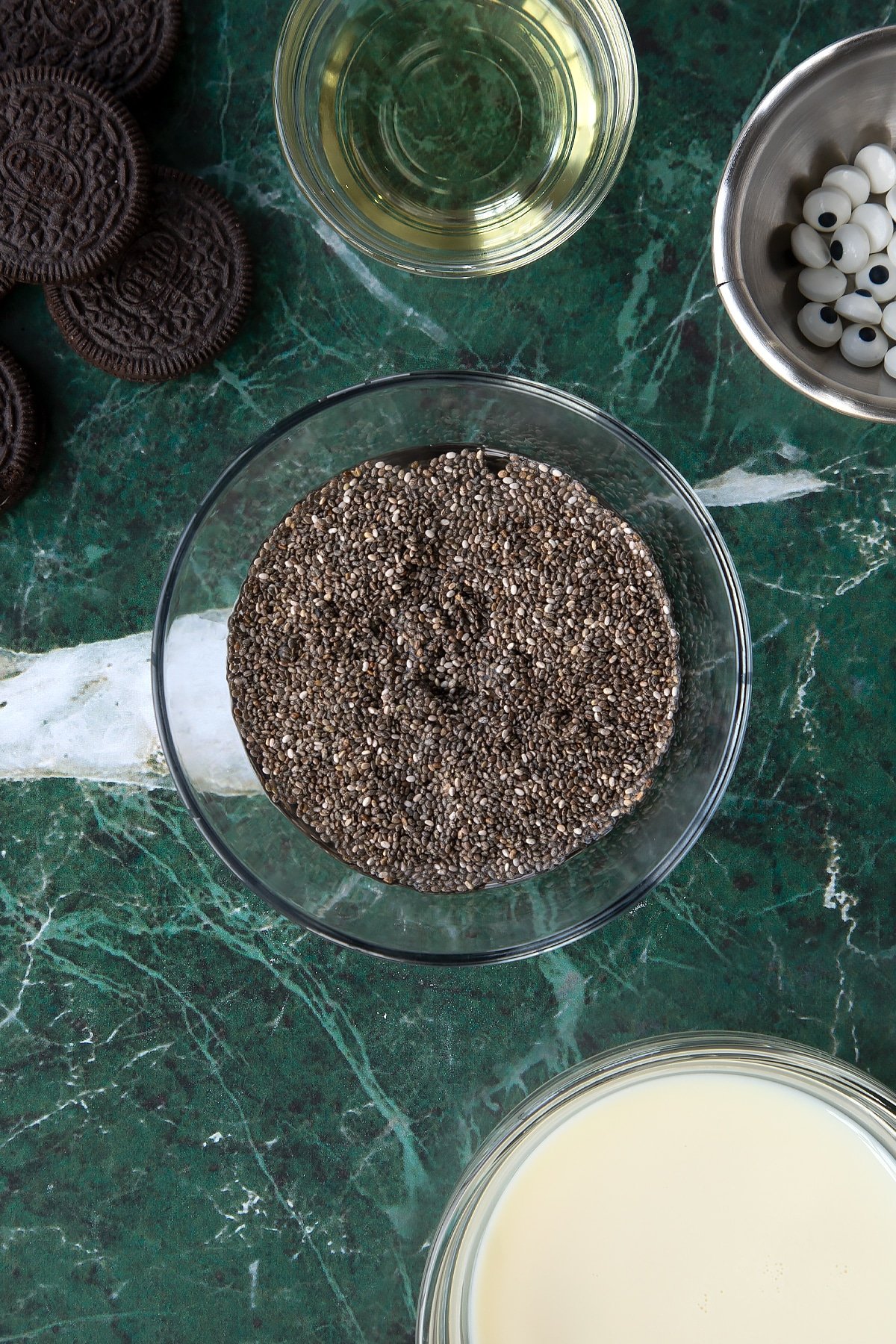 Chia seeds and water in a small glass bowl. Ingredients to make vegan Halloween cupcakes surround the bowl.