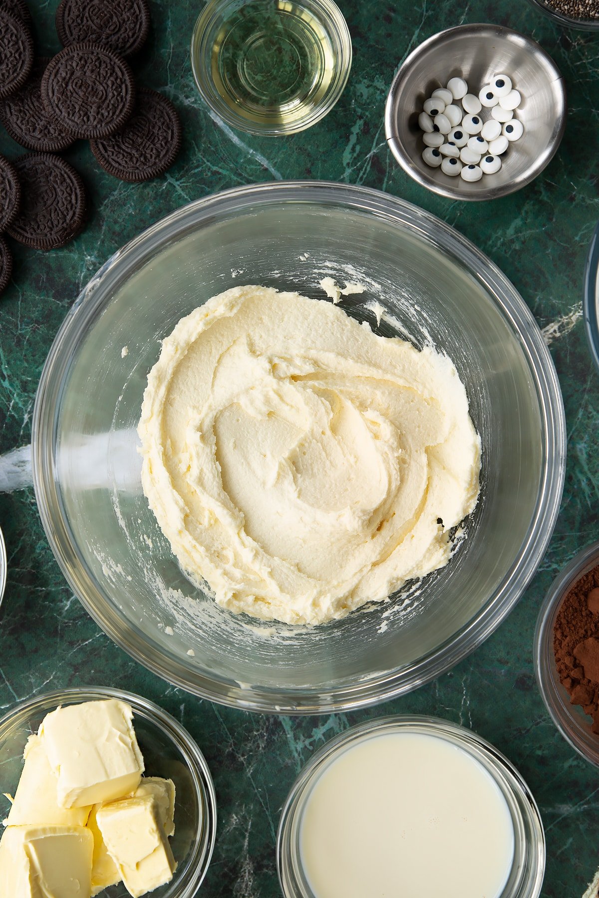 Vegan butter and caster sugar, beaten in a glass mixing bowl. Ingredients to make vegan Halloween cupcakes surround the bowl.