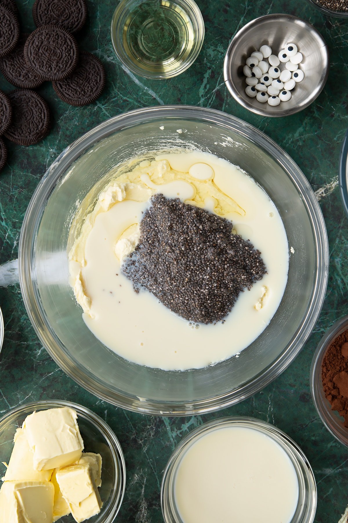 Vegan butter and caster sugar, beaten in a glass mixing bowl with chia "egg" and soya milk on top. Ingredients to make vegan Halloween cupcakes surround the bowl.