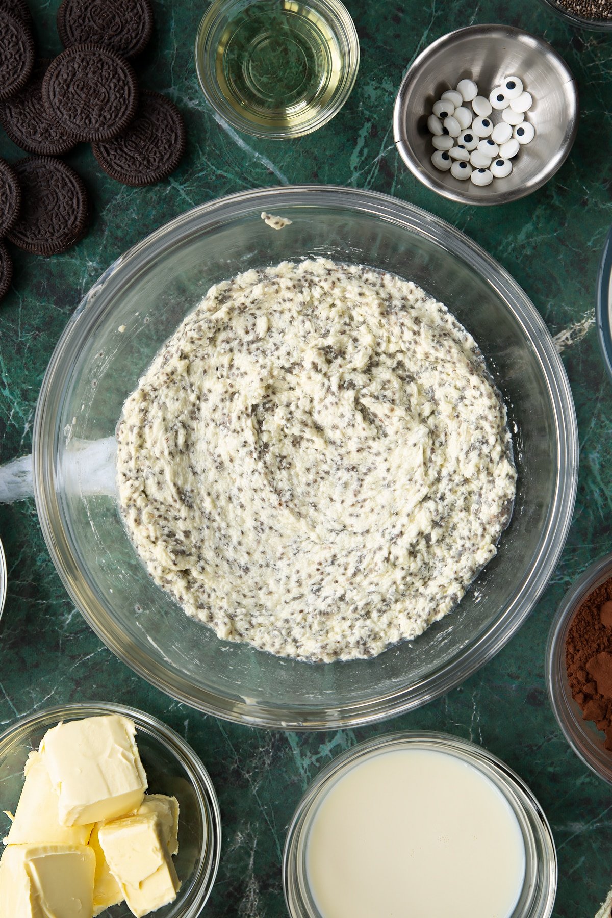 Vegan butter, caster sugar, chia "egg" and soya milk beaten in a glass mixing bowl. Ingredients to make vegan Halloween cupcakes surround the bowl.