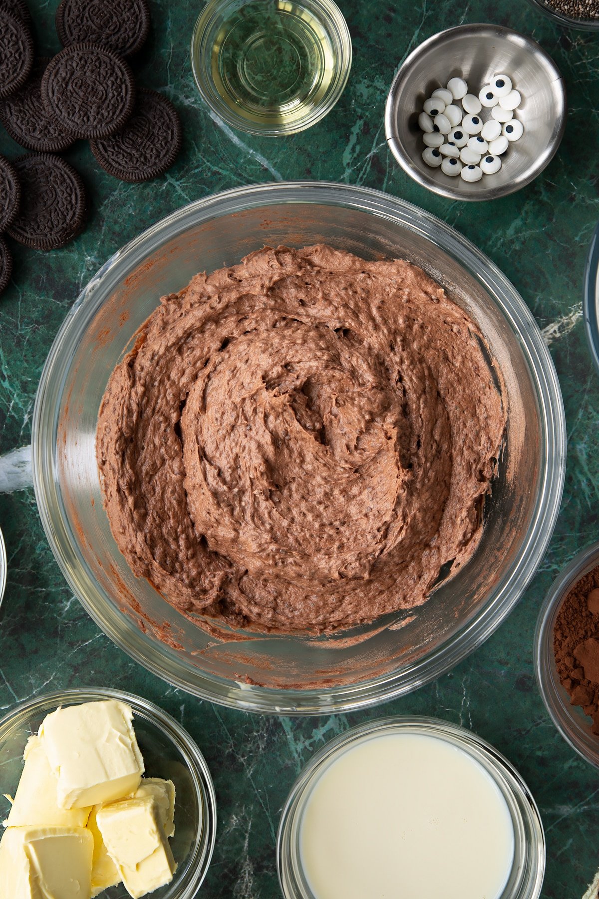 Vegan chocolate cake batter in a glass mixing bowl. Ingredients to make vegan Halloween cupcakes surround the bowl.