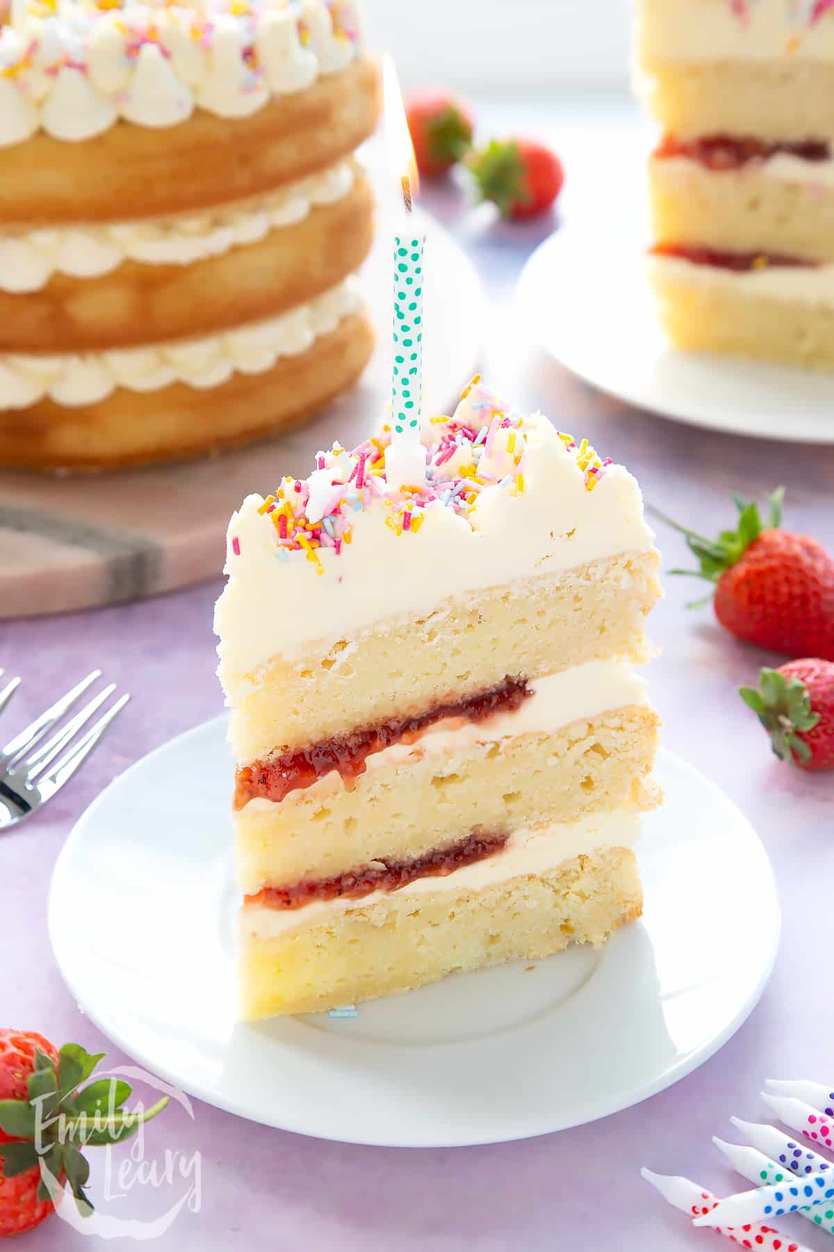 Slice of vegan birthday cake with a lit candle on a small white plate.