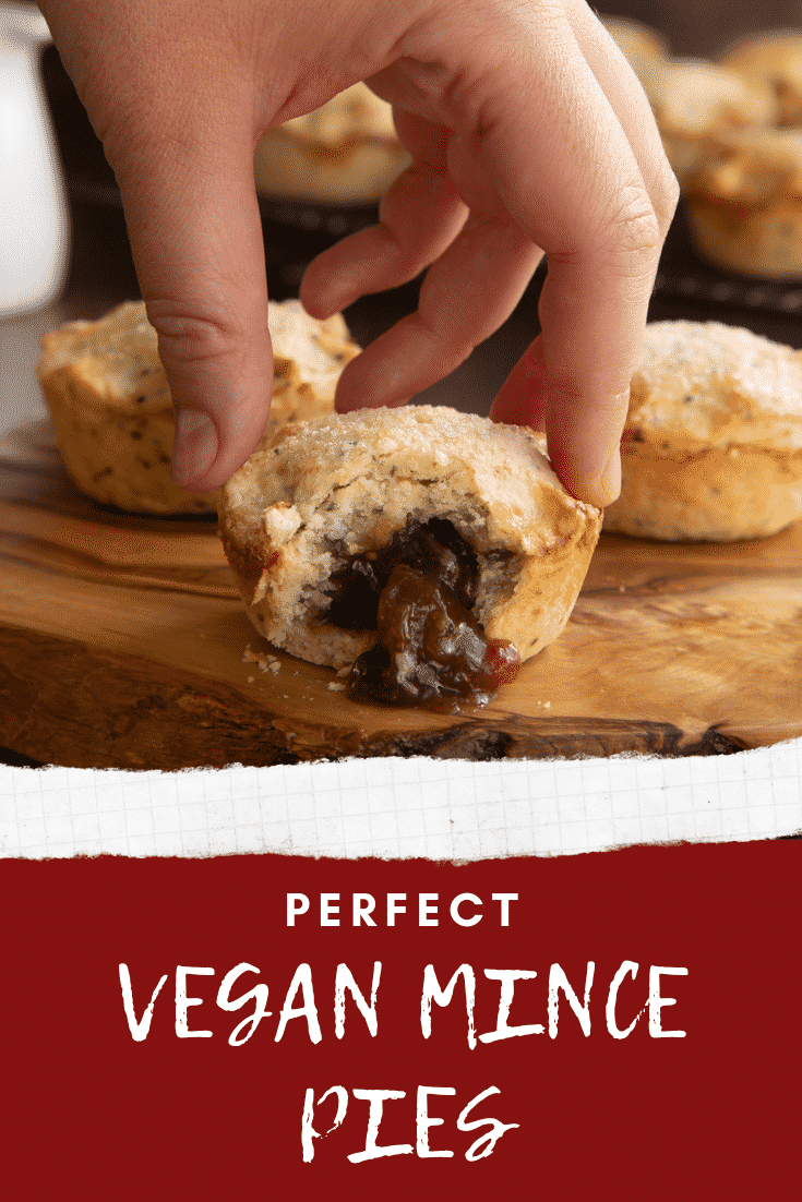 Vegan mince pies on a olive board with more on a wire rack in the background. One has been bitten open and a hand reaches for it. Captions reads: Perfect vegan mince pies