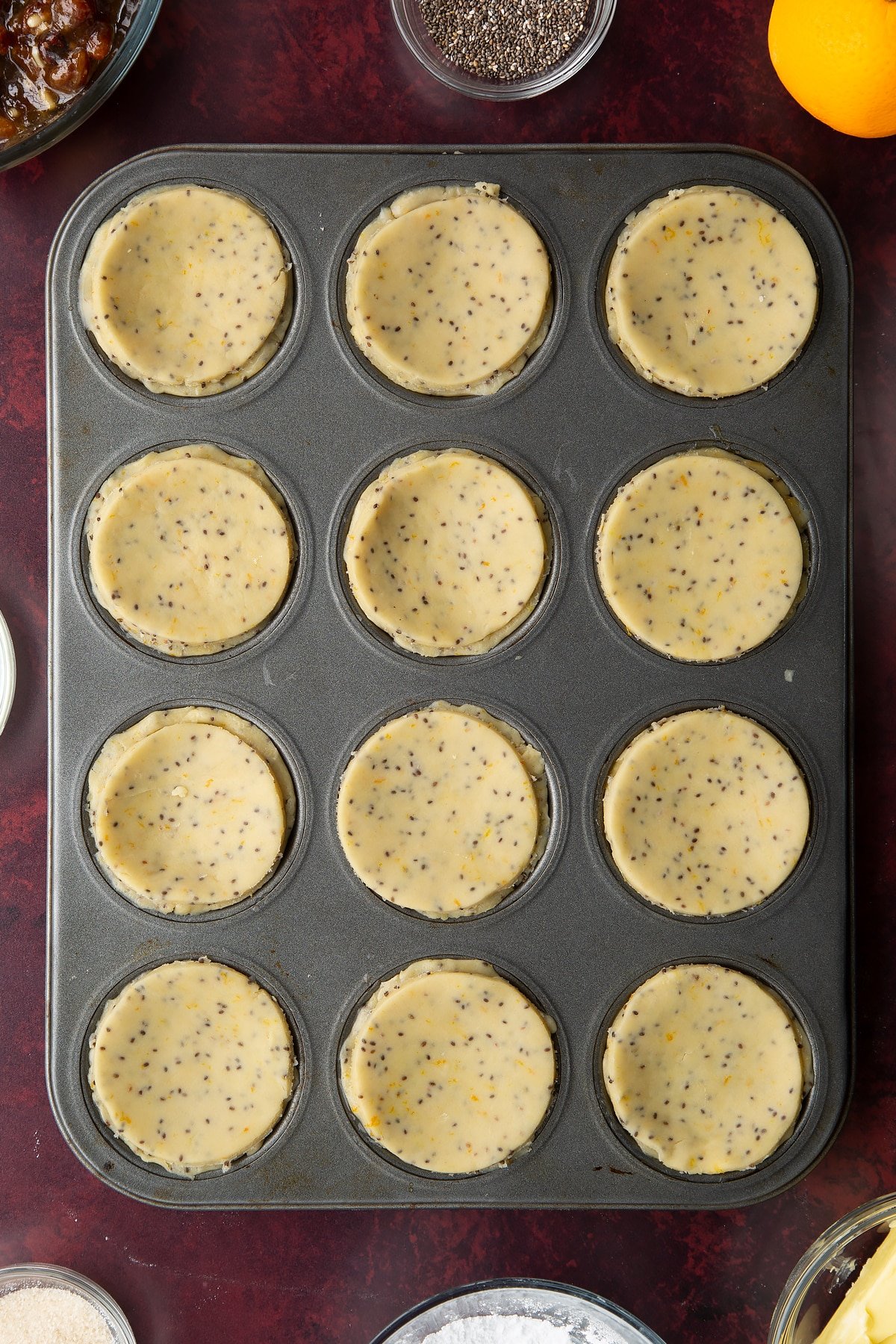 12-hole muffin tray lined with vegan pastry and filled with mincemeat and topped with pastry discs.