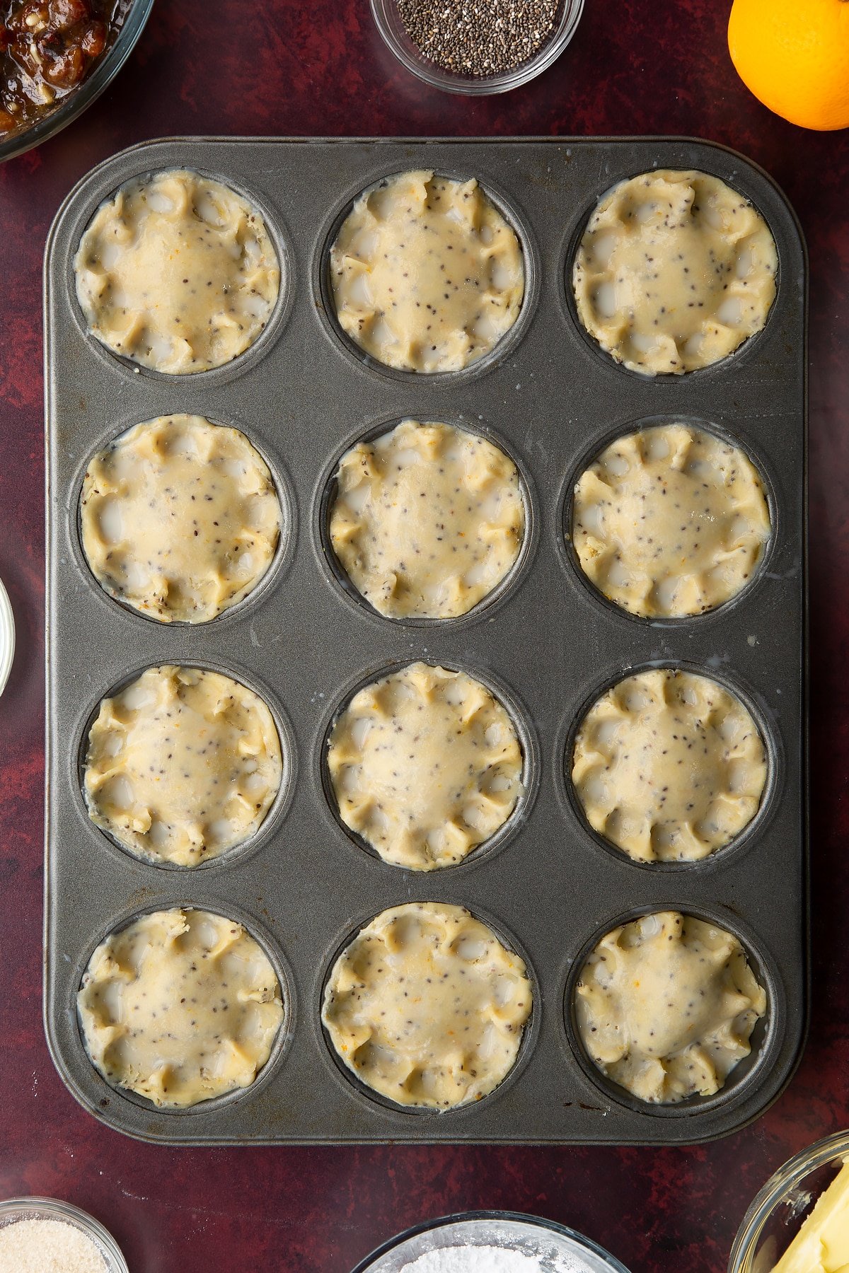 Uncooked vegan mince pies, brushed with milk in a 12-hole muffin tray.