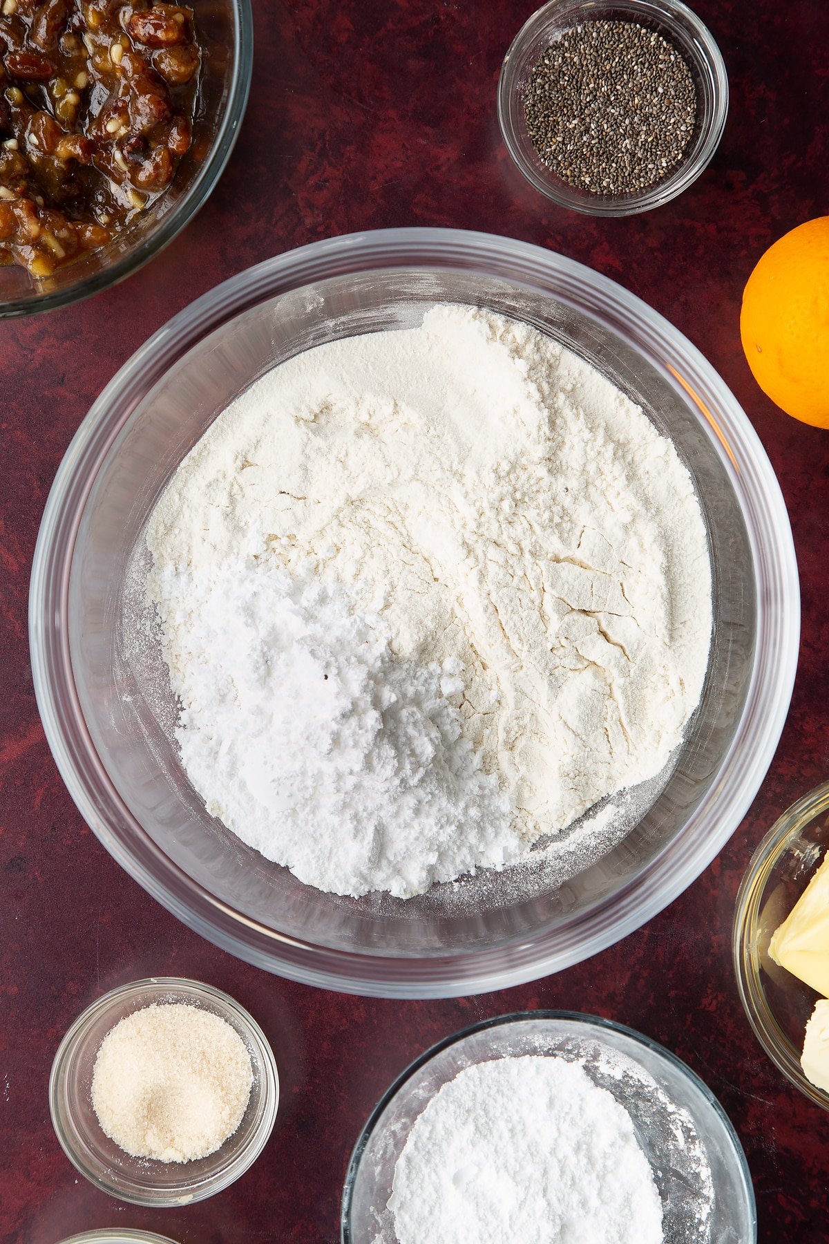 Flour and icing sugar in a mixing bowl. Ingredients to make a vegan mince pie recipe surround the bowl.