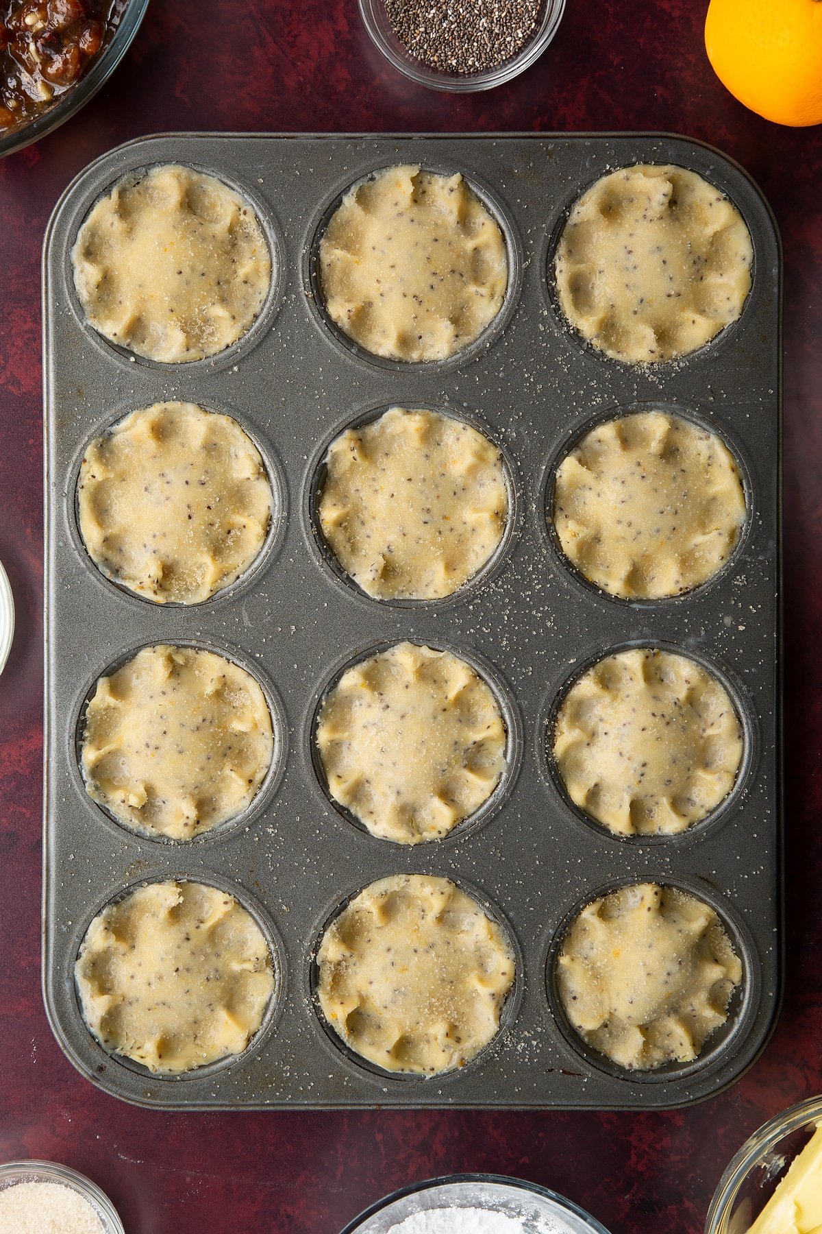 Uncooked vegan mince pies, brushed with milk and sprinkled with sugar in a 12-hole muffin tray.