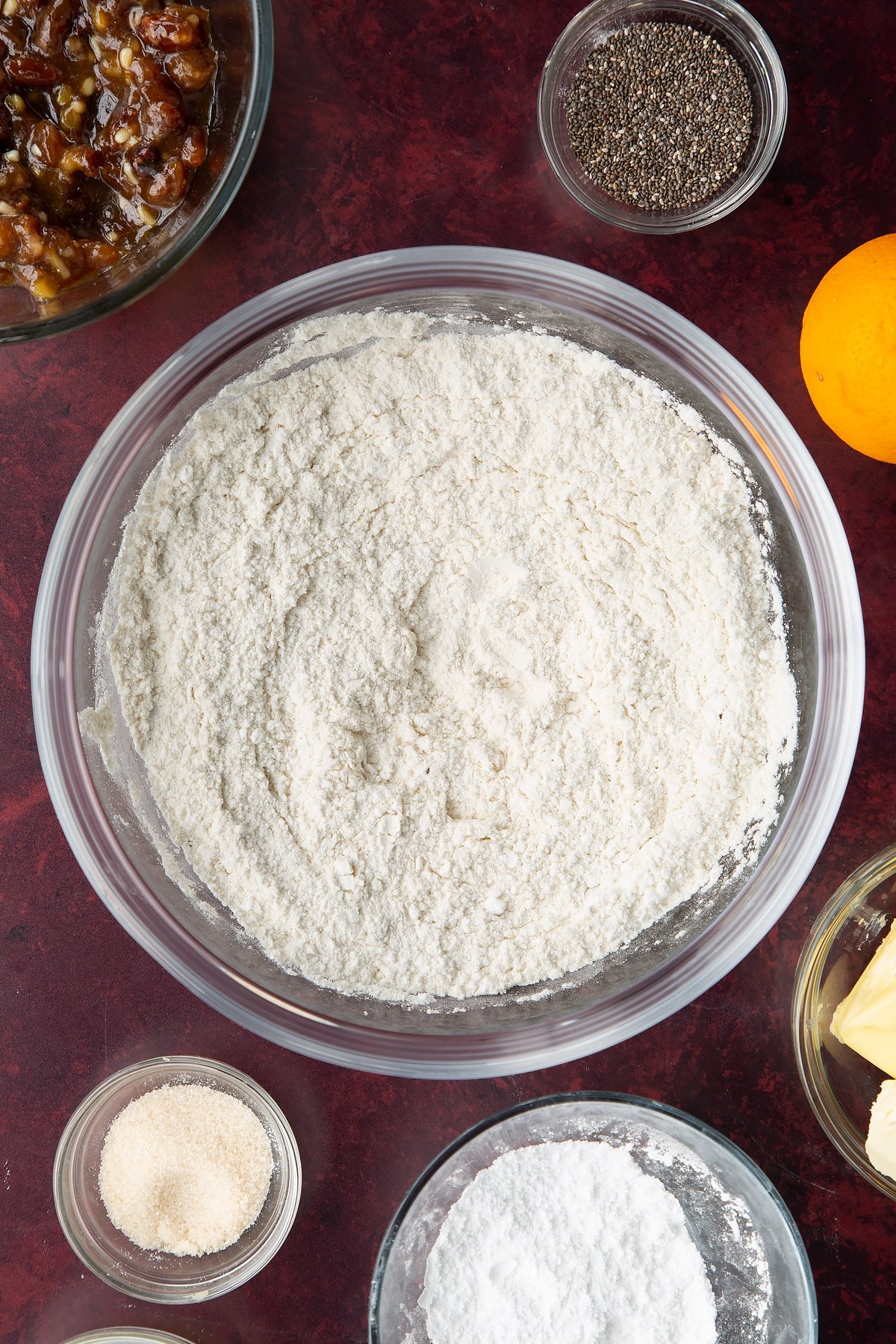 Flour and icing sugar mixed together in a bowl. Ingredients to make a vegan mince pie recipe surround the bowl.