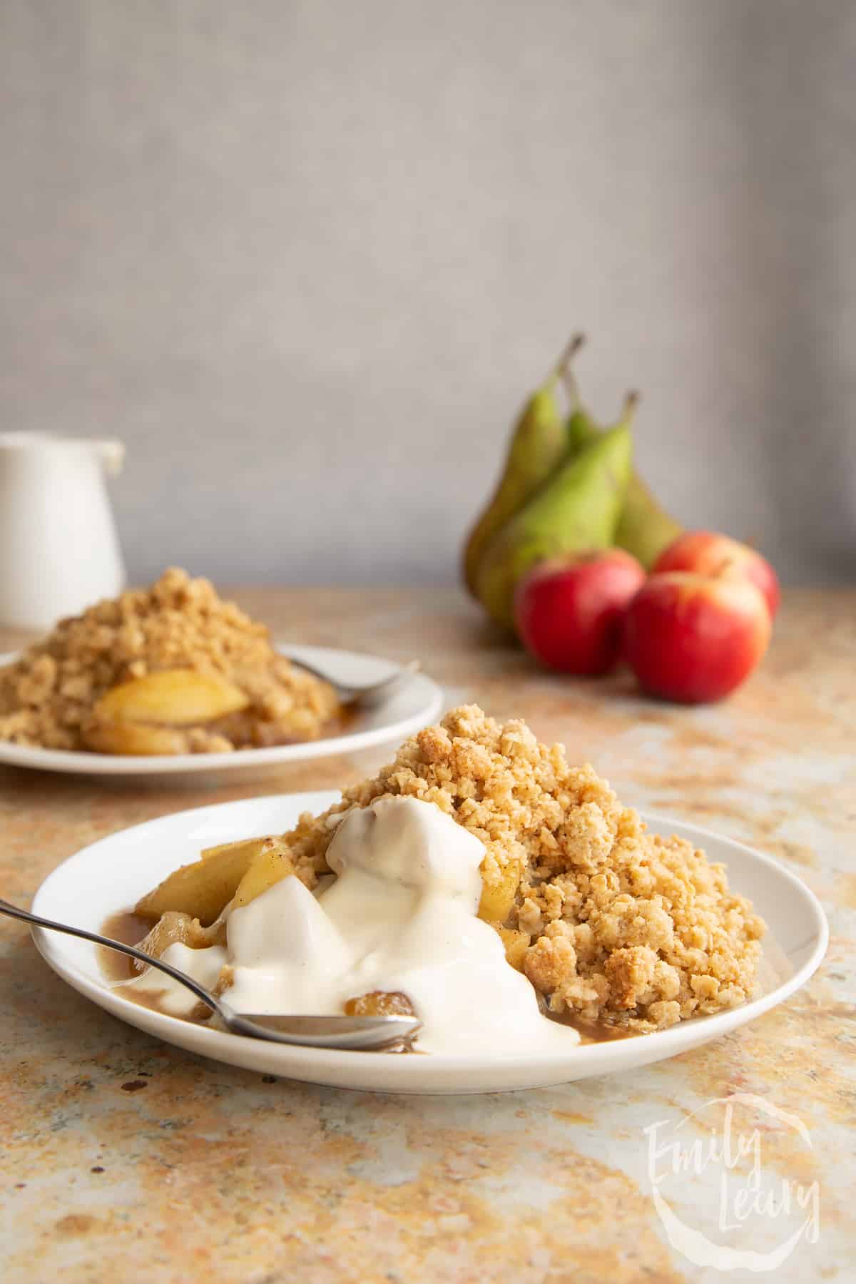 Apple pear crumble served to a small white plate with some custard and a small spoon.