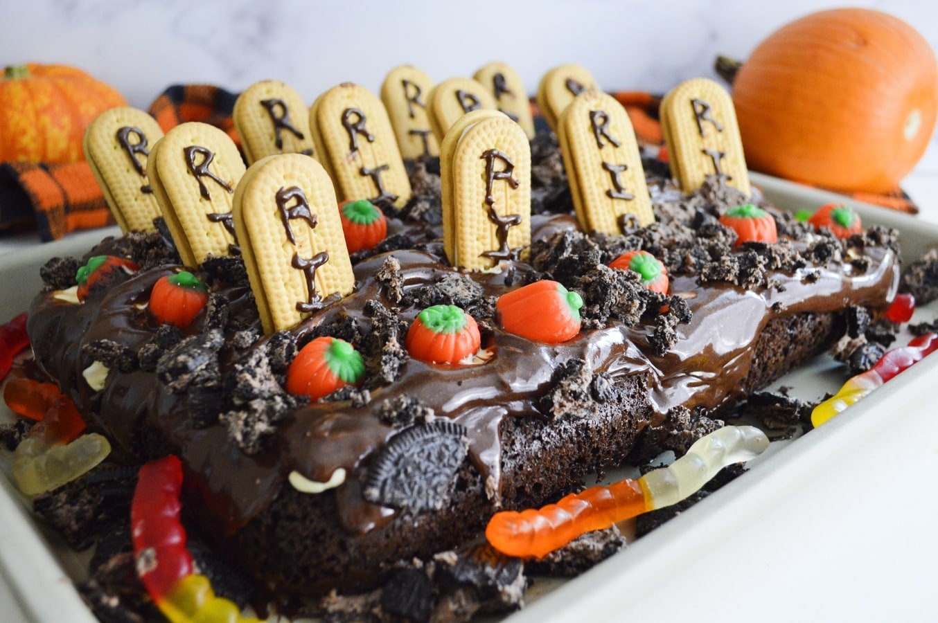A graveyard cake decorated with candy pumpkins and biscuit gravestones.