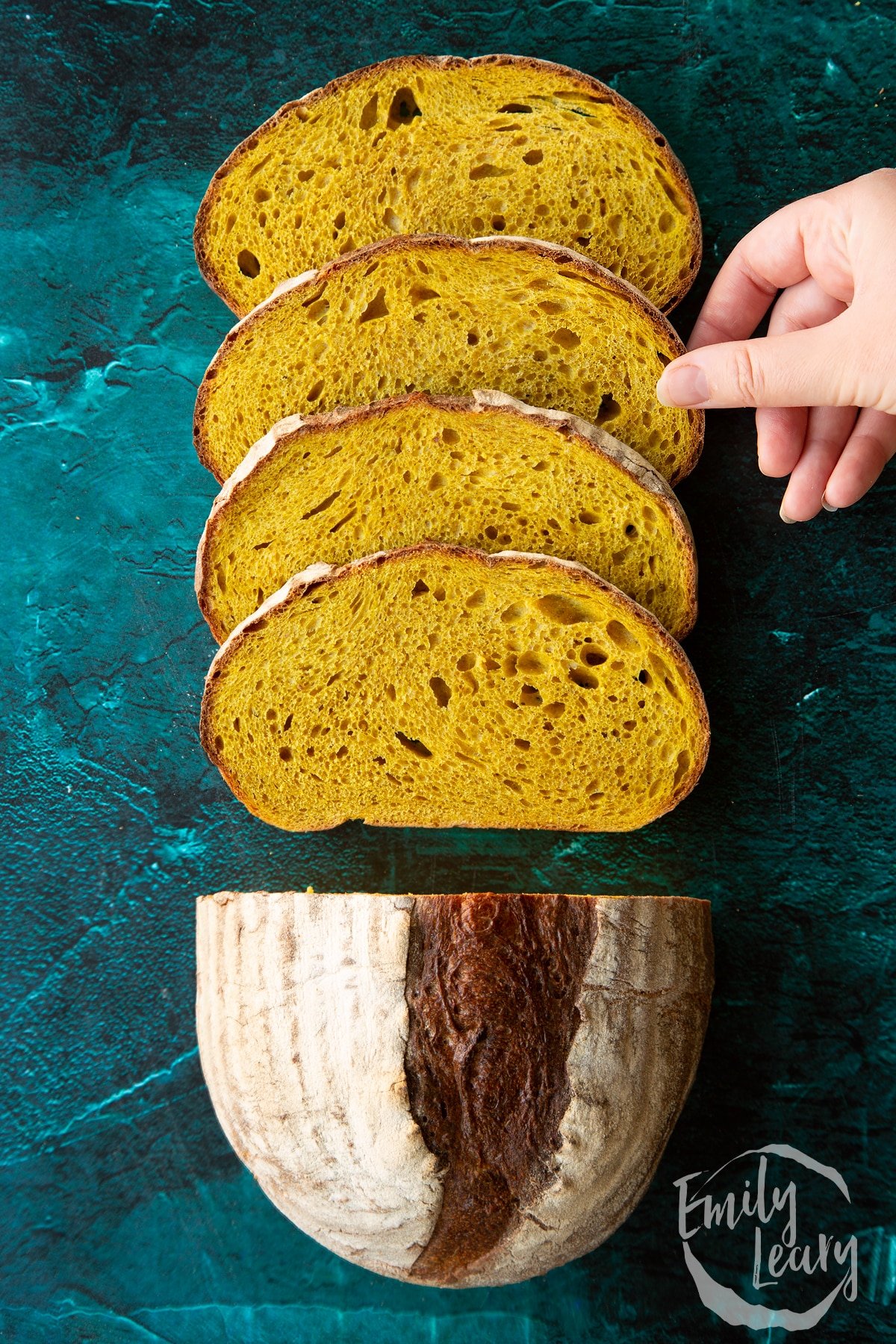 Pumpkin sourdough bread. Some has been cut into slices. A hand reaches to take a slice.