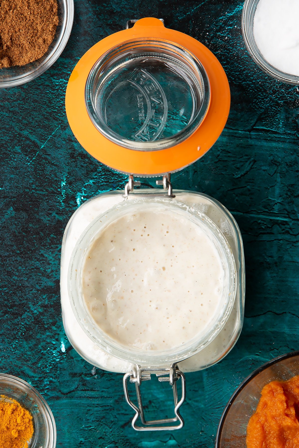 Sourdough starter in a jar. Ingredients to make pumpkin sourdough bread surround the jar.