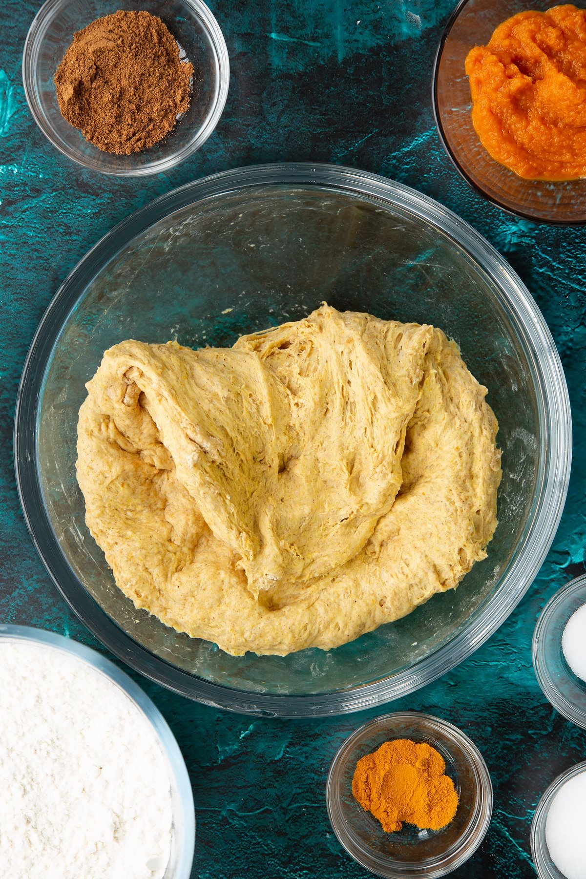 Pumpkin sourdough pressed into the base of a bowl. Part is folded over. Ingredients to make pumpkin sourdough bread surround the bowl.