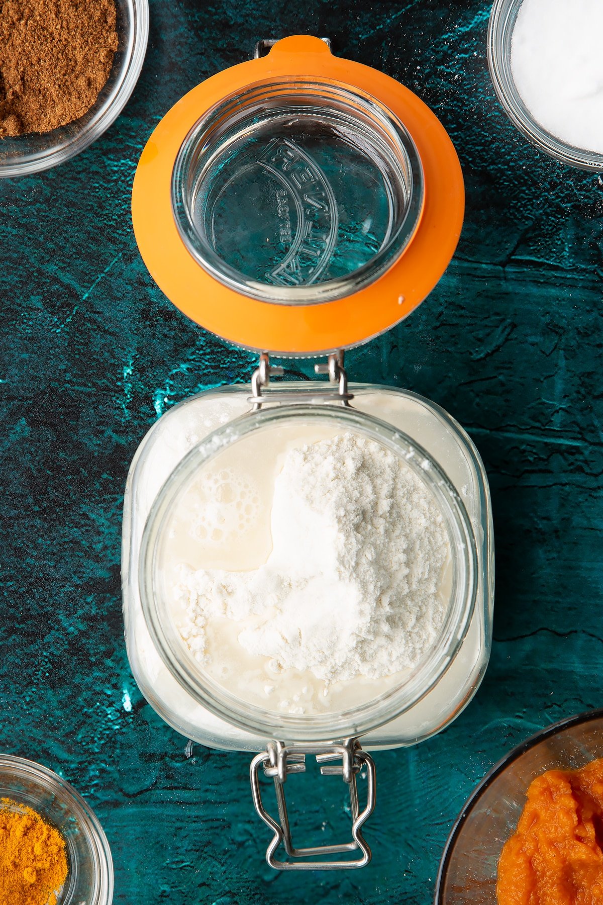 Sourdough starter in a jar with flour and water on top. Ingredients to make pumpkin sourdough bread surround the jar.