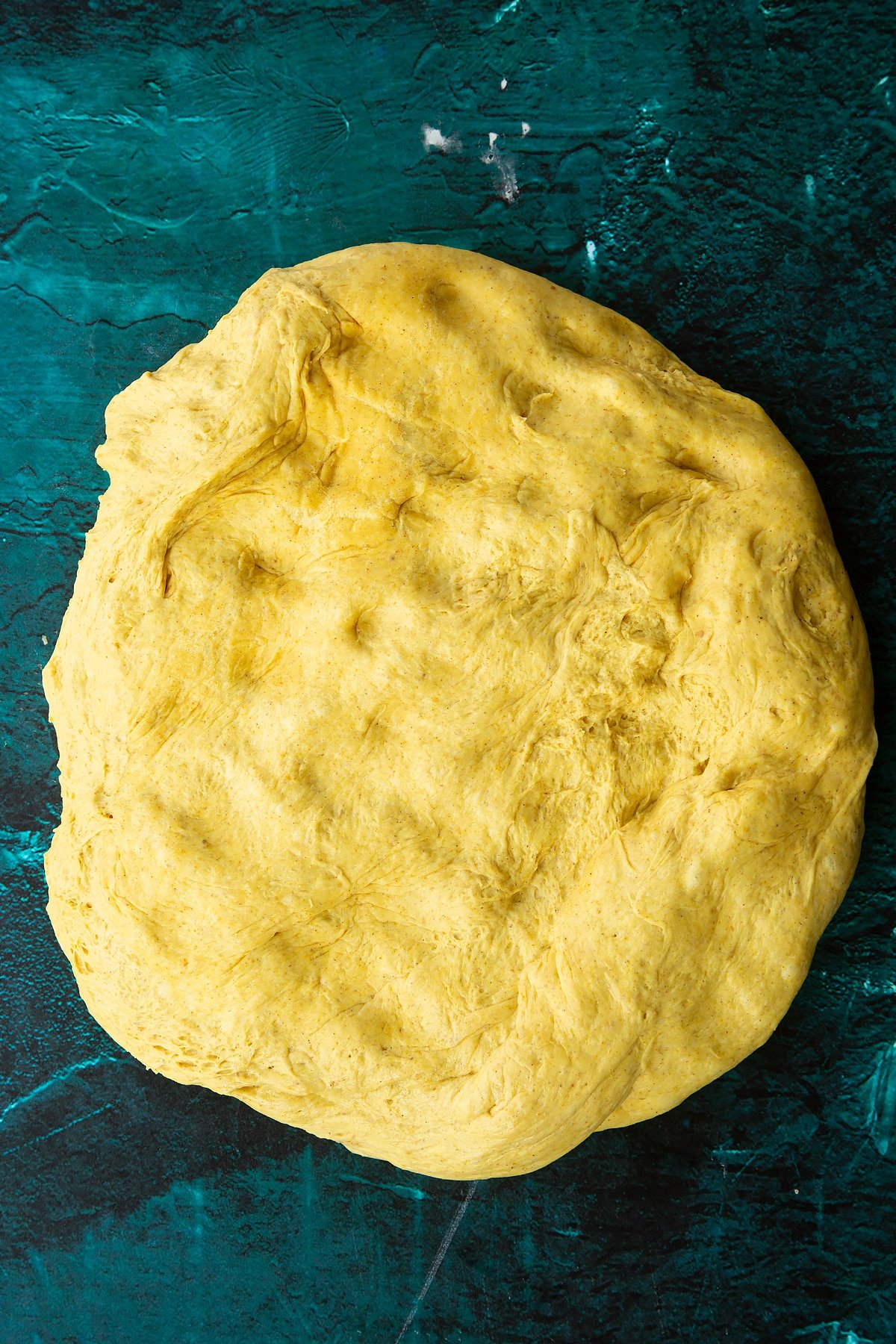 Risen pumpkin sourdough pressed into an oval onto a clean surface.