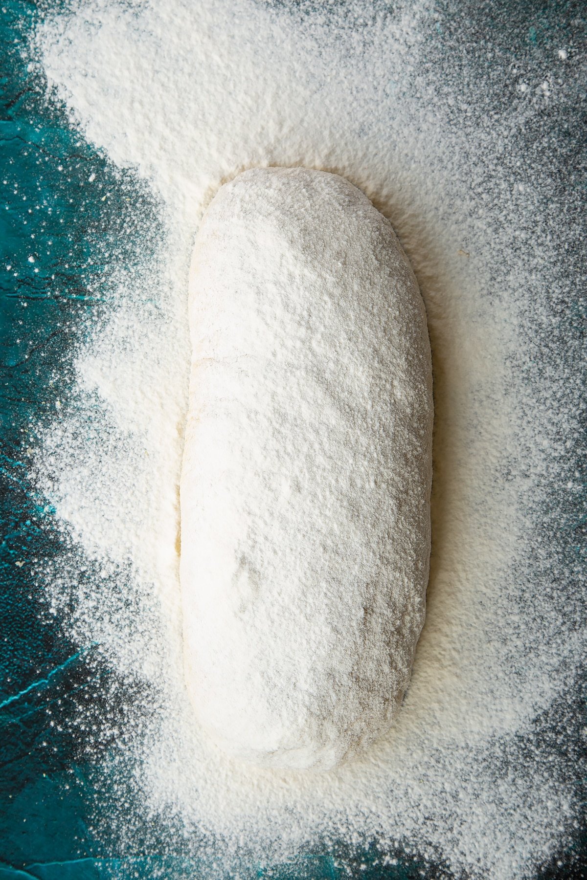 Pumpkin sourdough shaped into a sausage shape with a taut surface, dusted with flour.