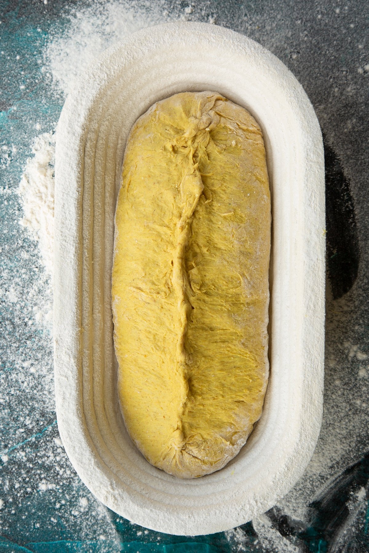 Pumpkin sourdough shaped into a sausage shape, placed top down in a floured proving basket. The seam has been pinched well to seal.