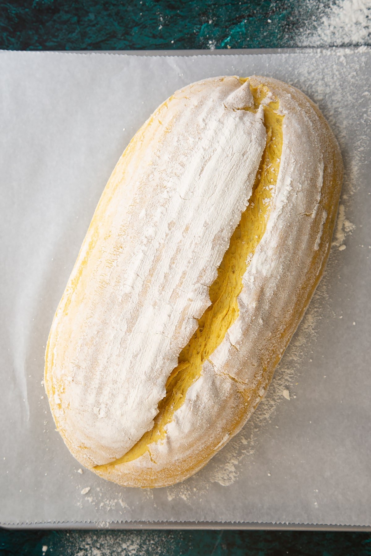 Shaped and risen pumpkin sourdough tipped out onto a baking sheet lined with baking paper. It has been slashed down the length.