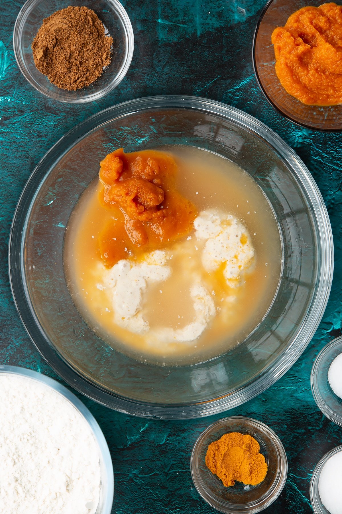 Pumpkin puree, warm water and sourdough preferment in a bowl. Ingredients to make pumpkin sourdough bread surround the bowl.