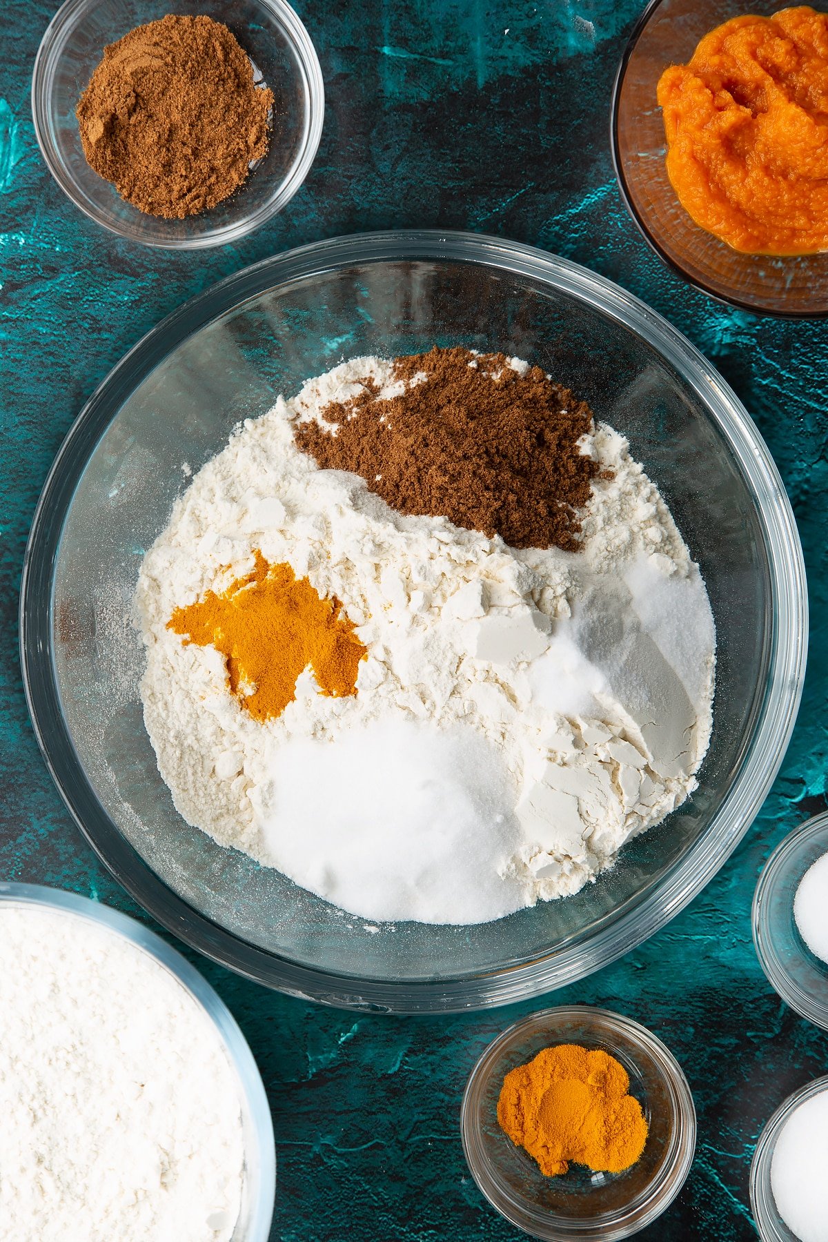 Flour, sugar, salt, mixed spice and turmeric in a bowl. Ingredients to make pumpkin sourdough bread surround the bowl.