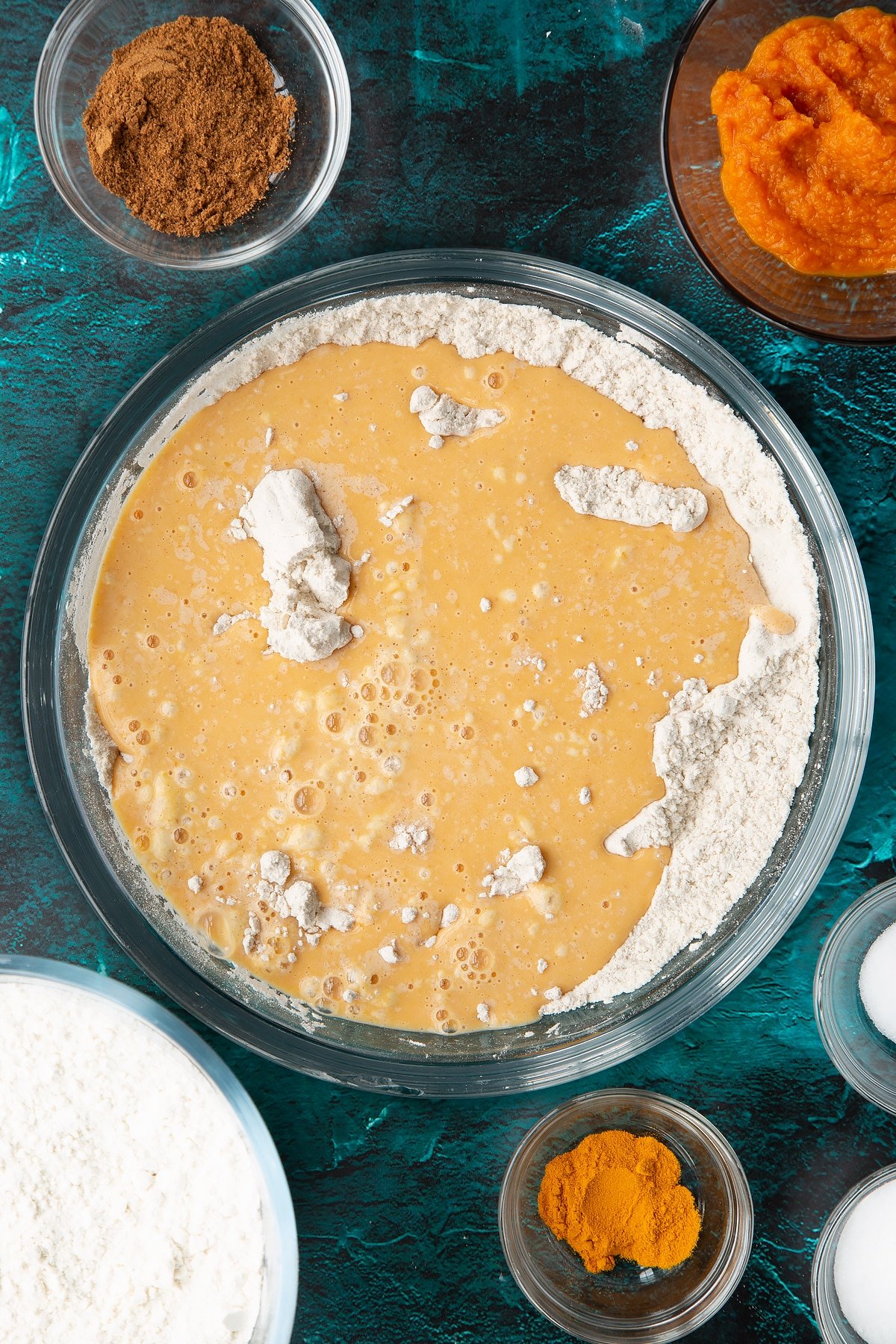 Sourdough pumpkin starter in water on top of flour and spices in a bowl. Ingredients to make pumpkin sourdough bread surround the bowl.