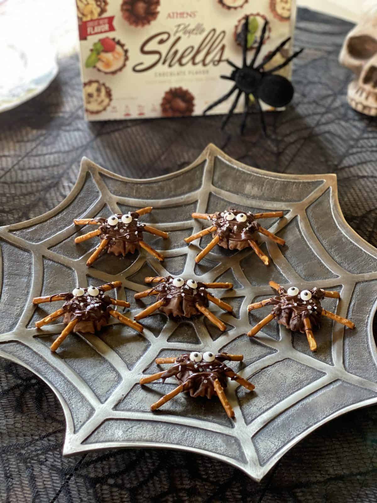 Edible spiders on a plate with chocolate bodies and pretzel legs.