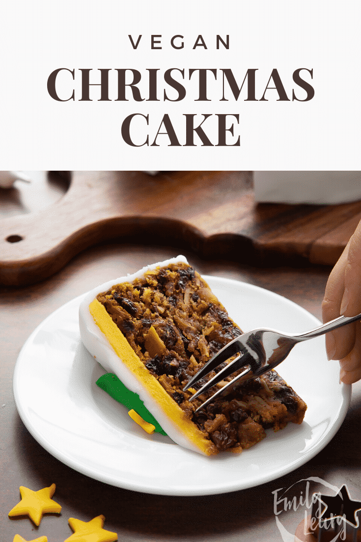 Slice of vegan Christmas cake on a white plate. A fork delves in. Caption reads: Vegan Christmas cake.
