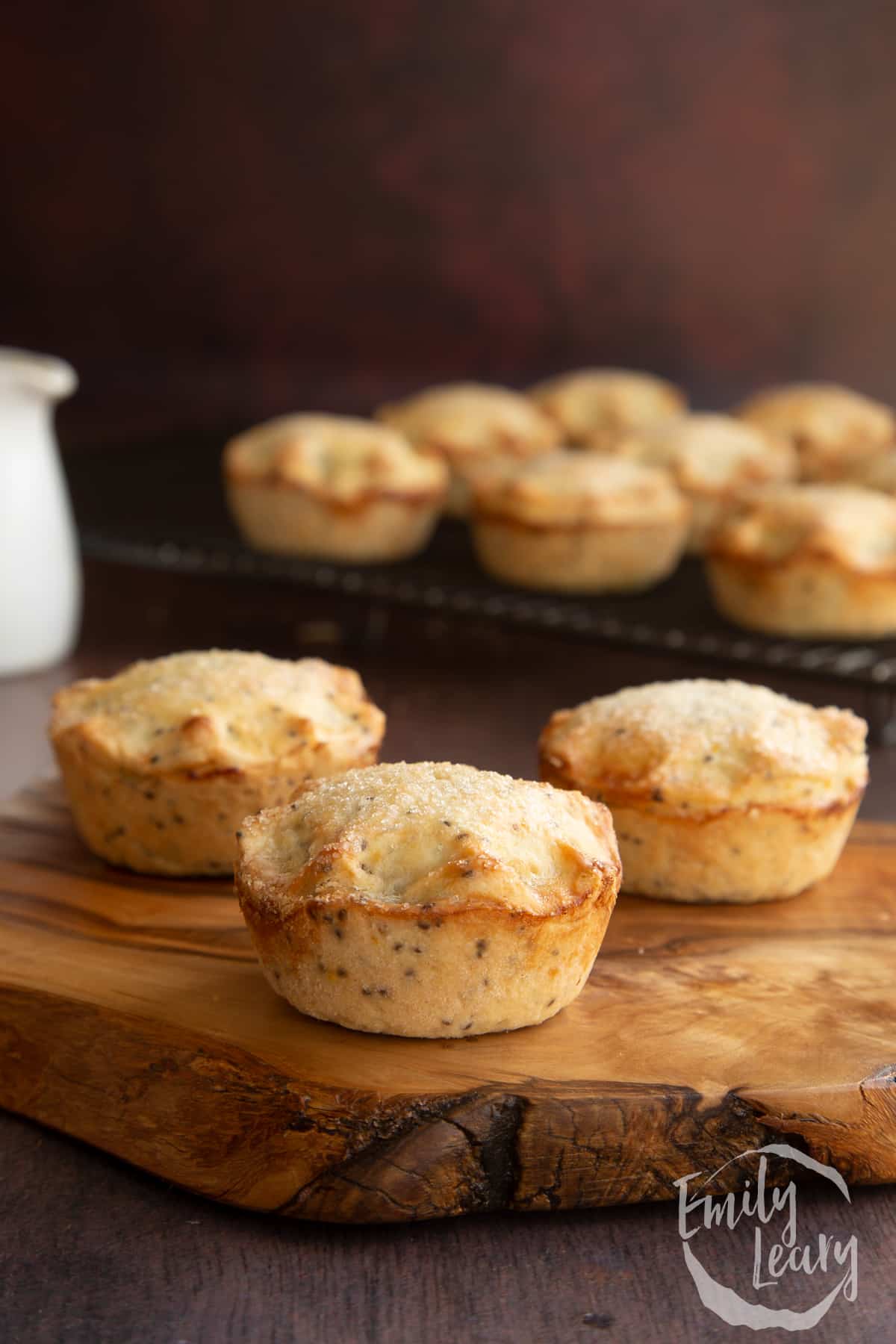 Vegan mince pies on a olive board with more on a wire rack in the background.