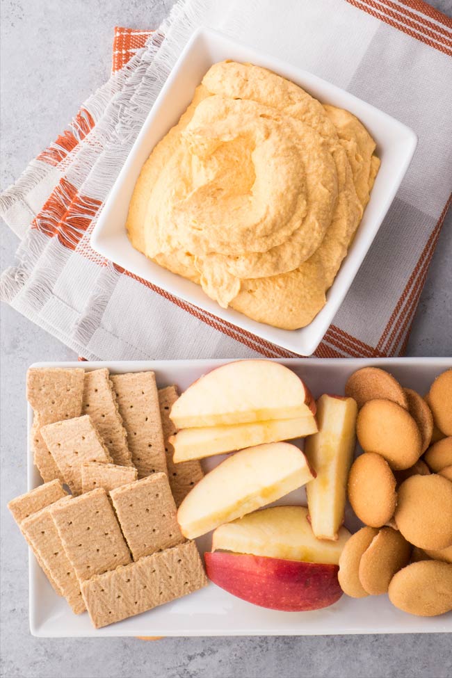 Whipped pumpkin dip served in a white, square bowl with fruit and cookies beside it.