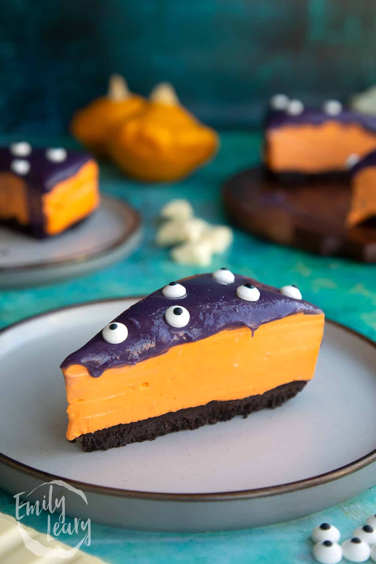 Slice of orange and strawberry Halloween cheesecake with an Oreo base on a plate.