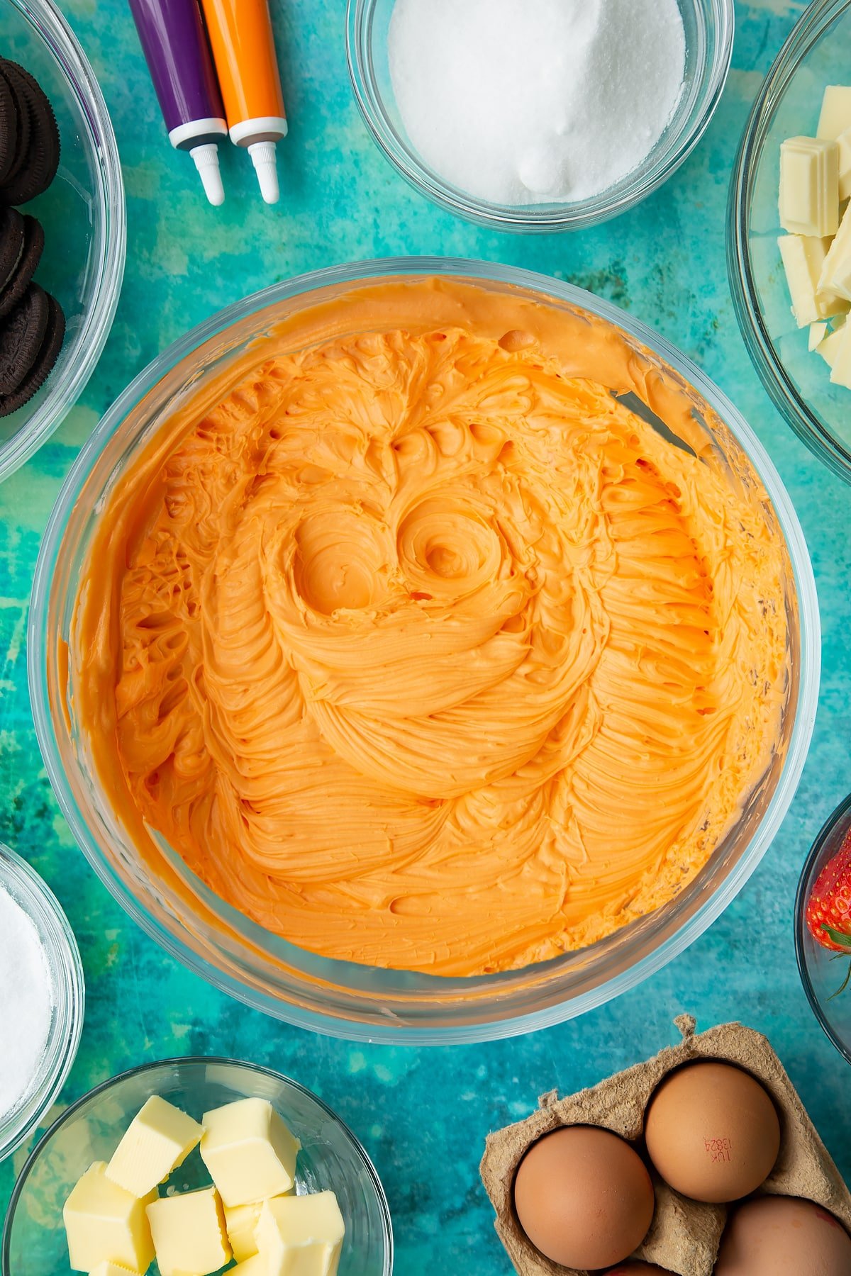 Orange cheesecake mix in a bowl. Ingredients to make Halloween cheesecake surround the bowl.