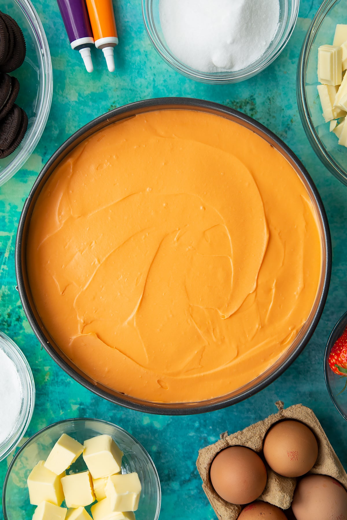 Orange cheesecake in a tin. Ingredients to make Halloween cheesecake surround the tin.