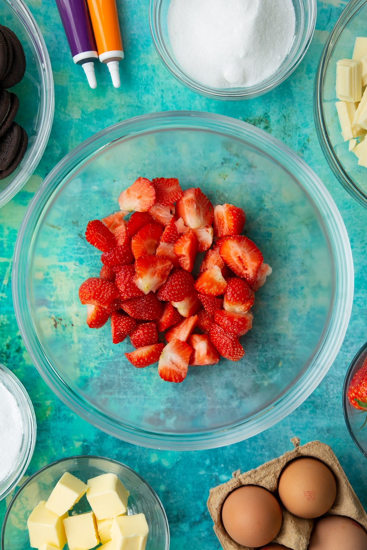 Chopped strawberries in a bowl. Ingredients to make Halloween cheesecake surround the bowl.