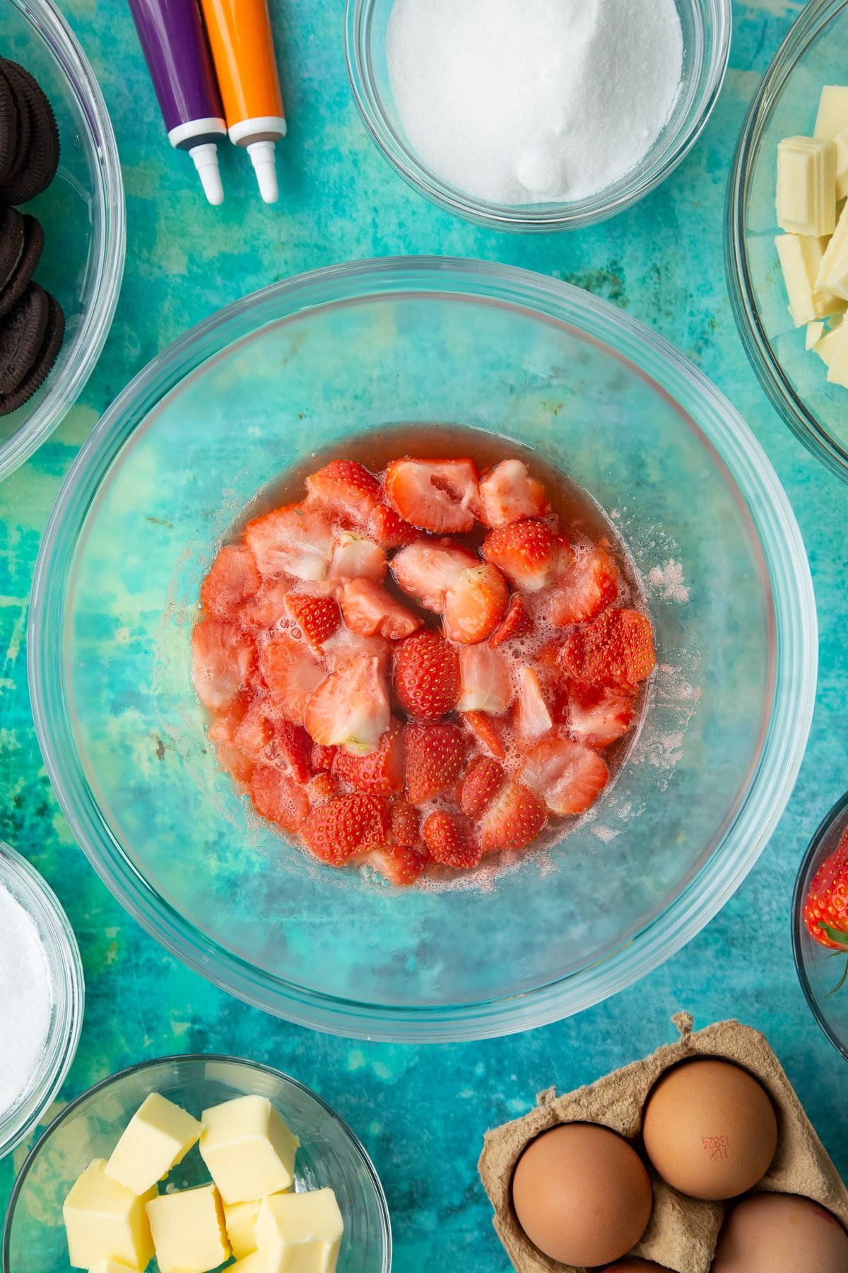 Cooked strawberries in a bowl. Ingredients to make Halloween cheesecake surround the bowl.