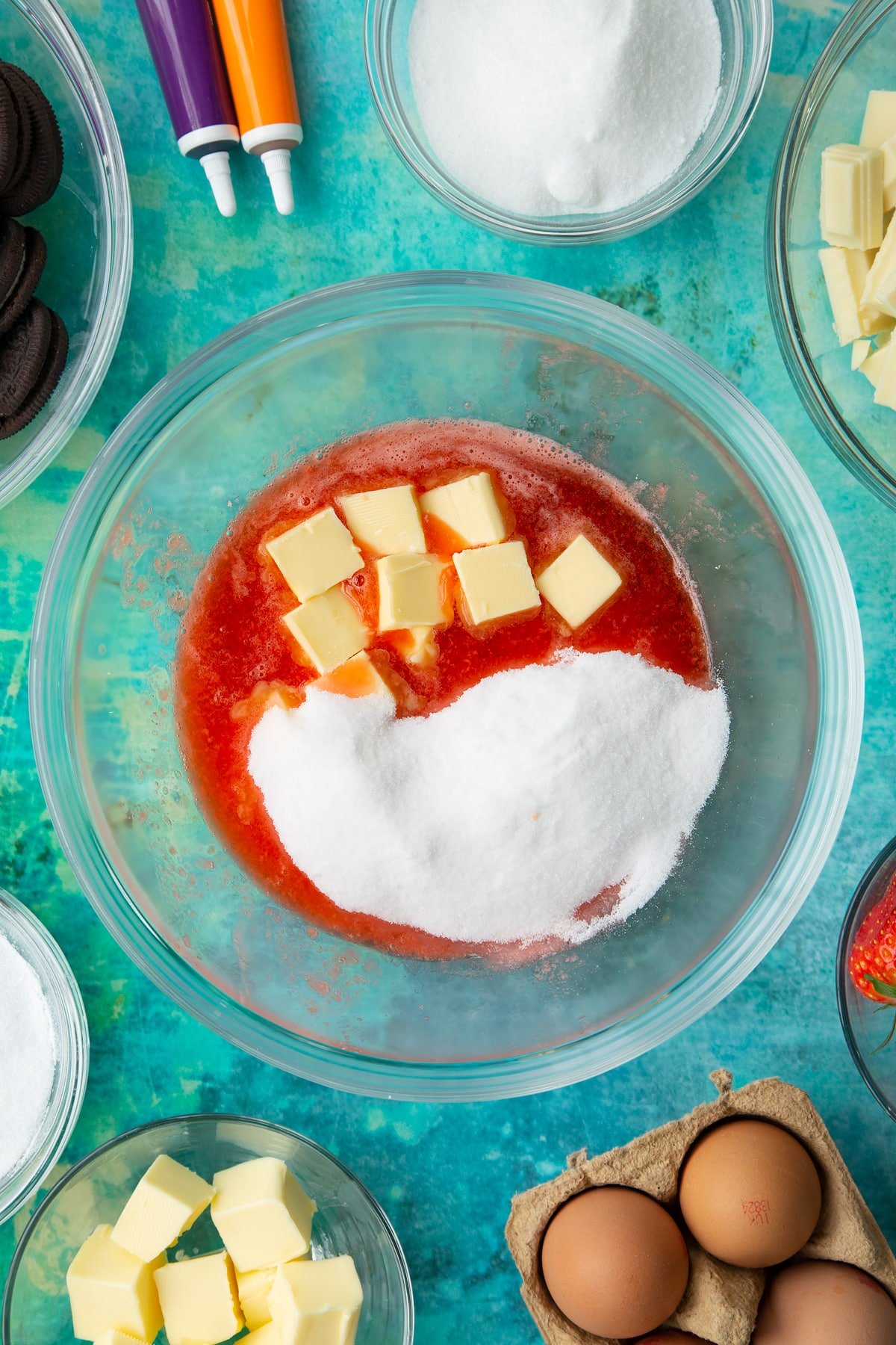 Strawberry juice, sugar and cubed butter in a bowl. Ingredients to make Halloween cheesecake surround the bowl.
