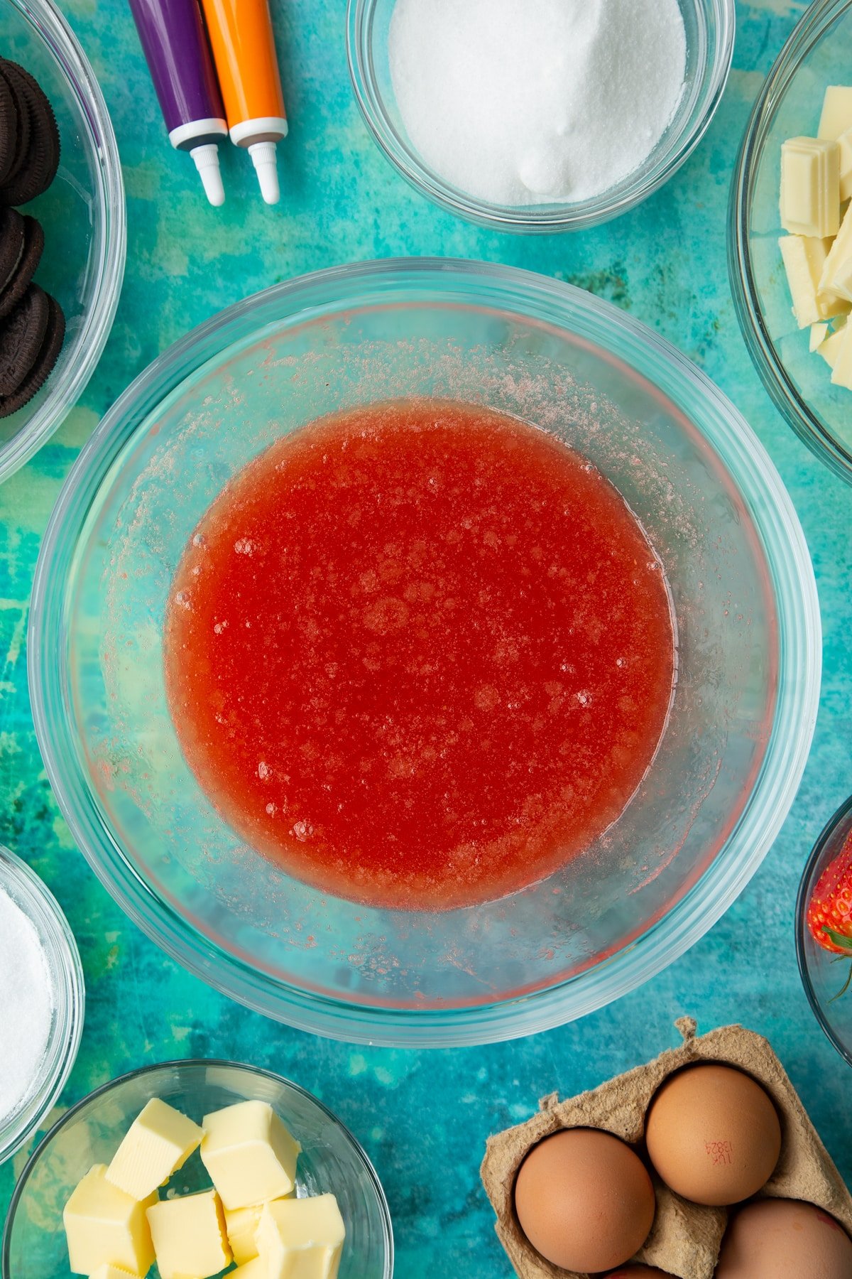 Strawberry juice, sugar and melted butter in a bowl. Ingredients to make Halloween cheesecake surround the bowl.