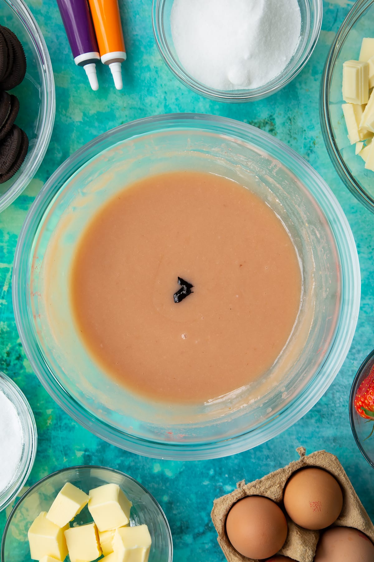 Strawberry curd in a bowl with a little purple dye in the centre. Ingredients to make Halloween cheesecake surround the bowl.