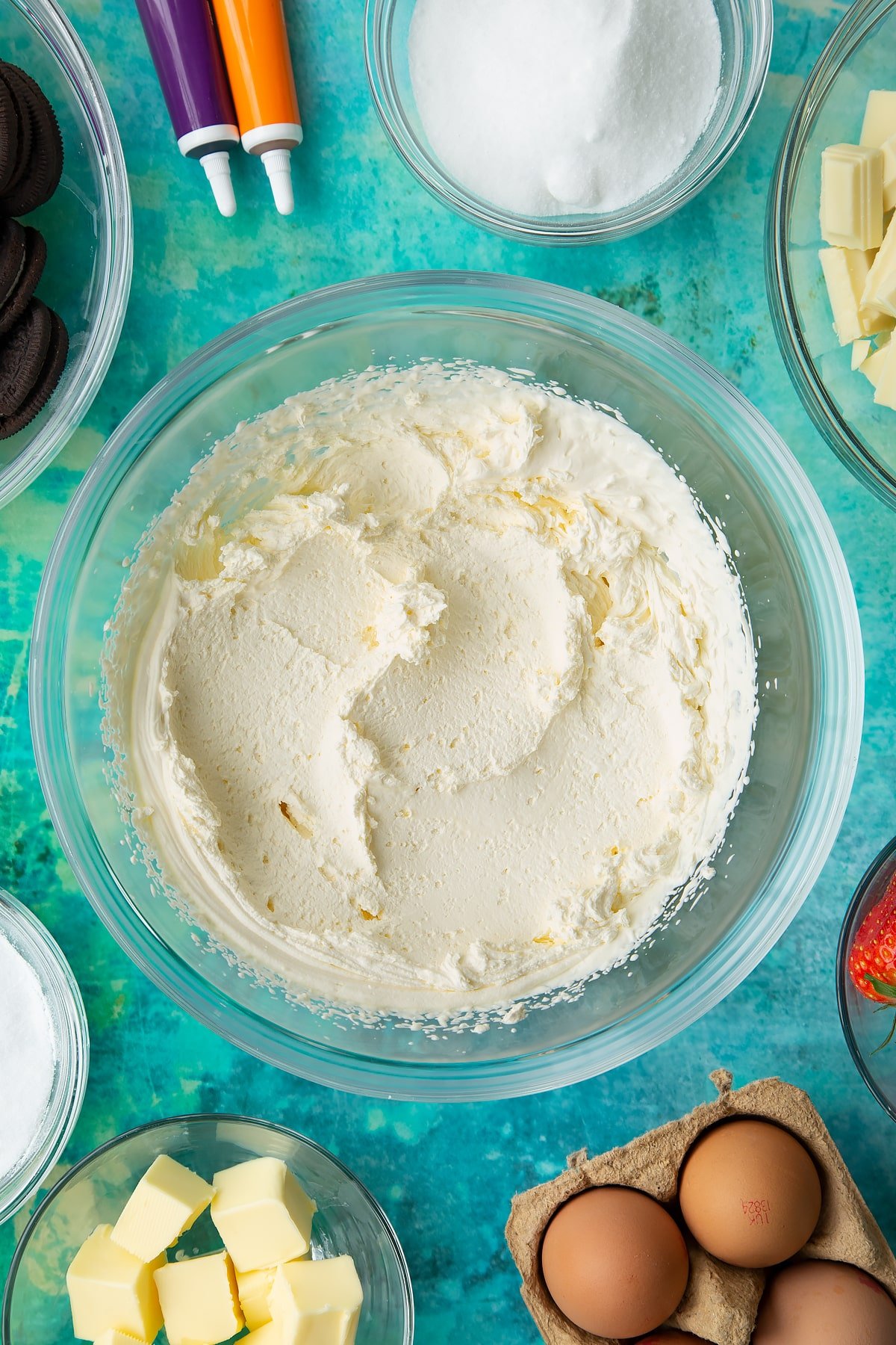 Whipped cream in a bowl. Ingredients to make Halloween cheesecake surround the bowl.