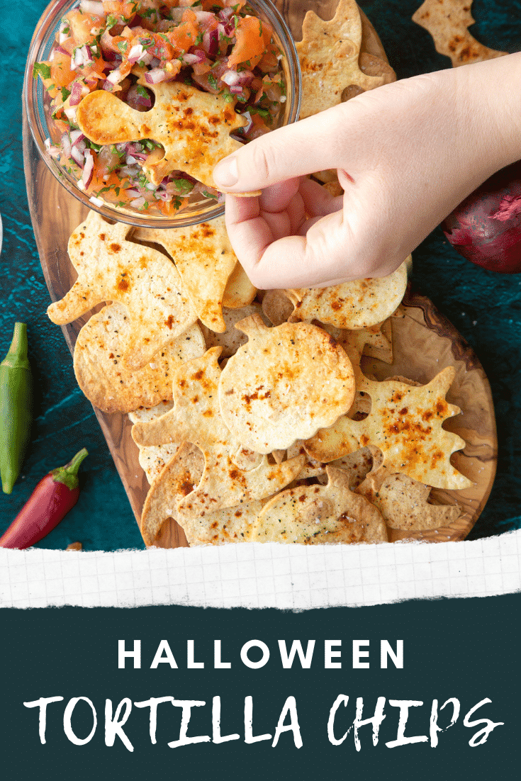 Halloween tortillas on a board with a small bowl of tomato salsa. A hand dips a ghost shaped chip. Caption: Halloween tortilla chips.