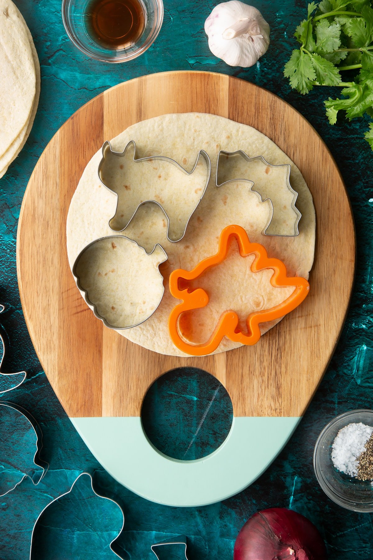 A soft, round tortilla on a board with cookie cutters on top.