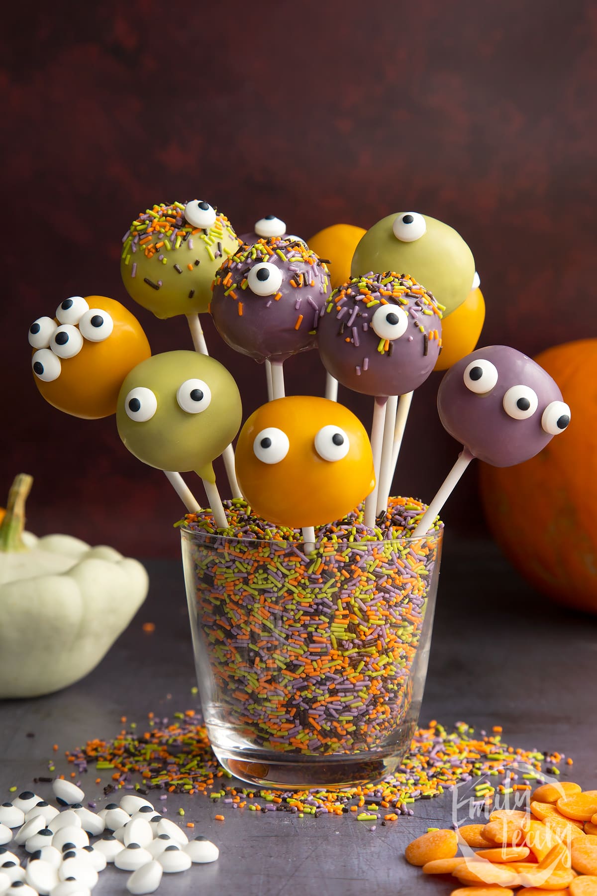 Halloween cake pops standing in a glass filled with Halloween sprinkles. 