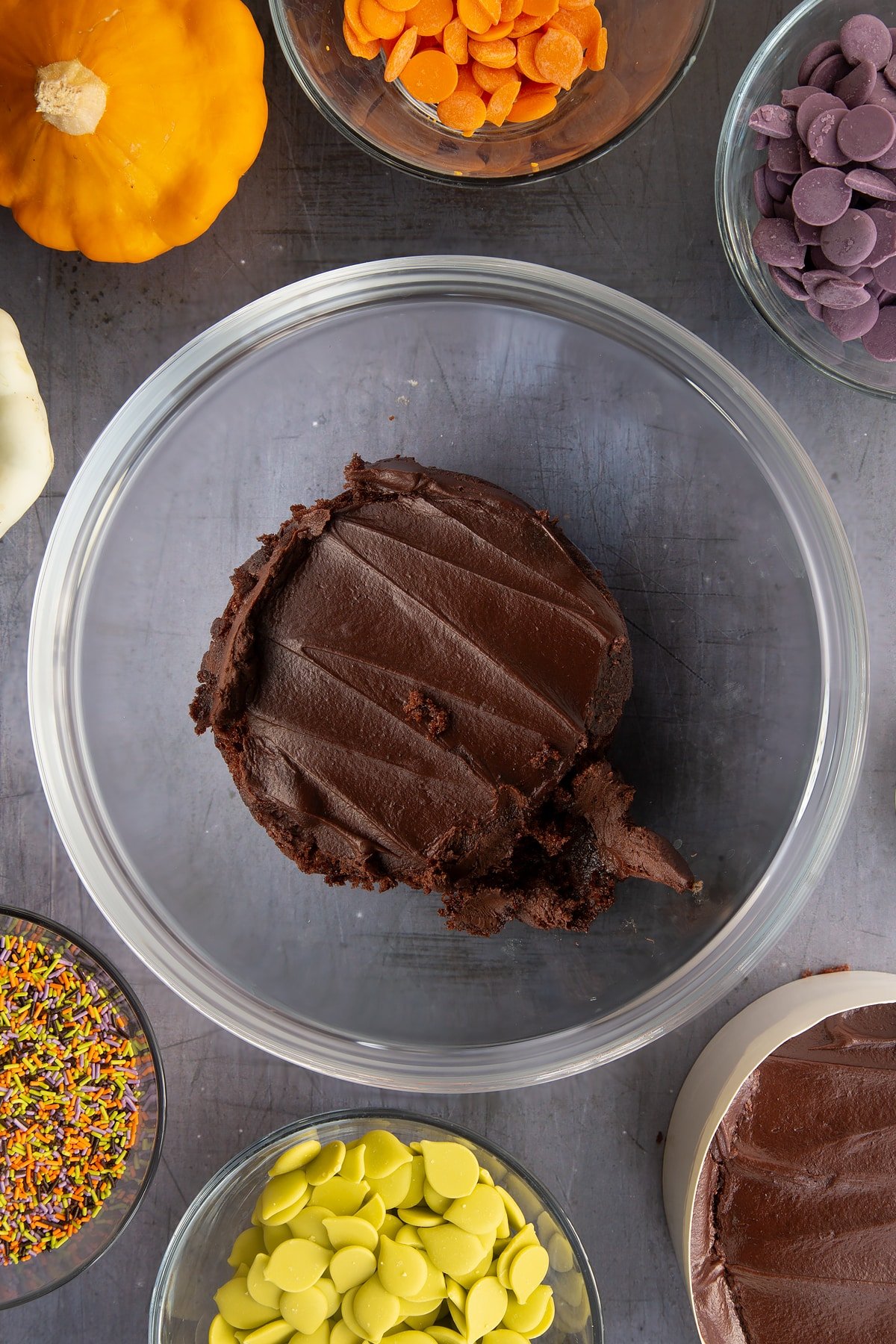 Chocolate fudge cake in a bowl. Ingredients to make Halloween cake pops surround the bowl.