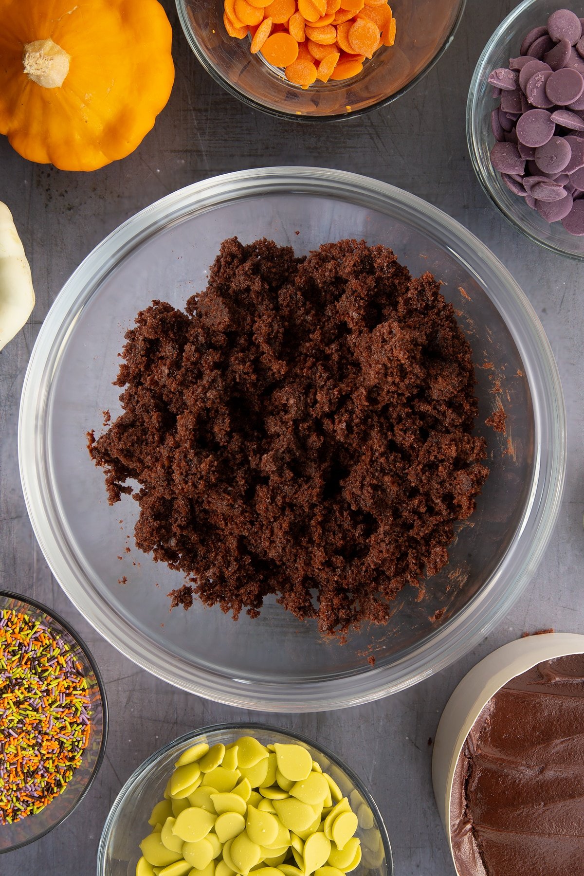 Chocolate fudge cake broken down in a bowl. Ingredients to make Halloween cake pops surround the bowl.