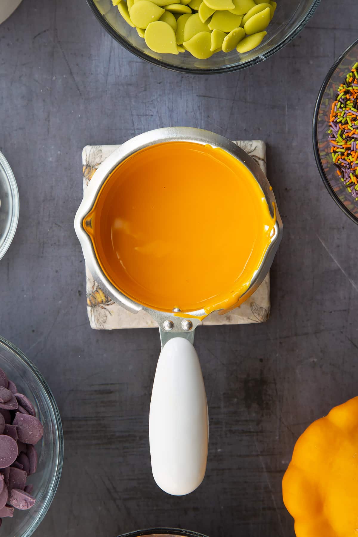 Orange candy melts in a little pan. Ingredients to make Halloween cake pops surround the pan.