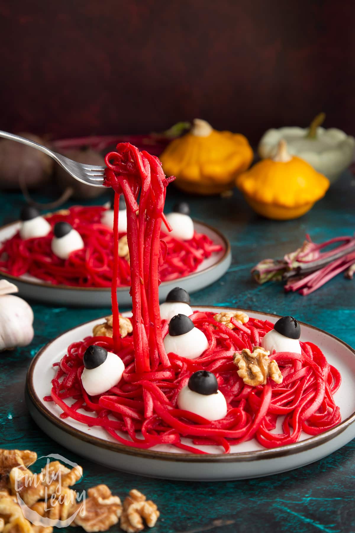 A plate with a beetroot Halloween pasta recipe, topped with mozzarella eyes and walnut brains. A fork lifts some pasta.